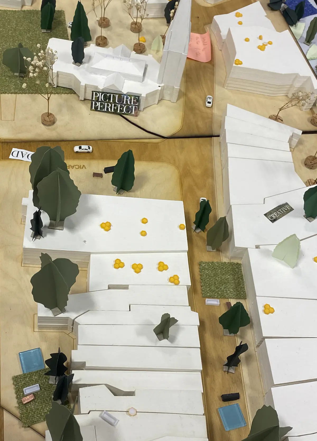 Looking to be the centrepiece of our exhibition, we proposed to create a site model of Dudley Highstreet at 1:200 scale with buildings modelled in a simple form. Local residents and visitors to the exhibition are then invited to decorate a chosen building to how they would envision it sat within the context of a greener Highstreet. We want to tie in our themes of biodiversity and materials by proposing that buildings can, and do, have the potential to be a lot healthier, sustainable, and interactive on the street. This site model also helps gain vital public opinions on the Highstreet and prompts discussion of areas most in need of attention.

To ensure that the model is utilising the MDF to the most efficient standard possible. First, the centres of the massing blocks have been hollowed out. This allows a reduction in materials used as other buildings can be cut in the centres of the model. Then the top is finished with a solid piece.
The waste material is placed into the recycling rack where other students can reuse it; otherwise, if the material left cannot be used for another project, it is recycled correctly by the university.

The model spanned just over 3.4m long and over 50cm wide. With the majority being cut from scrap woods that would fit the jigsaw of the shape, we were able to drastically cut down on waste. We also got some small benches and bee hives printed from recycled plastics, and used dried flowers as trees to represent the green spaces. Ultimately, the model seemed like a huge success, and really helped portray our ideas about Dudley High Street to those who came by. Everyone from Dudley who saw the model knew that it was the High Street, and interacted well with it. The size did make it difficult to move, especially to carry to the site, but it sat nicely in the centre of the the room and really drew people in to interact with it.

The model brought people in from outside to play with, write on, interact with. It became a spectacle for the public to come in and see what was happening and offer their ideas about what could be done.

The event was a success. Many people from the public (those who heard about the event, and those who just happened across it on the day) came in to interact with the model, which sat as the centre piece in the room. Kids liked to play with the pieces while the adults talked about things that could come from actions to help the High Street, not just leave it as is.

SOME OF THE KEY IDEAS WERE:
- The Shops need to be inviting for everyone. It’s no good having these places to go if people would rather take a bus to the next town.
- Just putting up boards across the windows is awful. Paint, Posters, Graffiti: Anything that actually makes the High Street look still alive is better than just wooden boards.
- More Green is needed. While it is obvious that there is a lack of Trees, many people wanted to push for these small bushes or planting spaces that could easily be implemented across the street.
- Spaces for public events or for people to at least gather at. While there is the Market and Fountain, it is not enough for the people of Dudley.
- Something needs to be done about the cars on the High Street. Some were Pro-Removal of all Cars, while some just wanted to limit when they could access the High Street.

Following the exhibition we created a series of drawings with our own interpretation of Sarah Wigglesworth ‘The Dining Table’ drawing. The drawings are a perfect representation of the our interactive model at the ERA Environmental Exhibition and Event. Showing the interaction the public had with the model, as well as the conversations that were held around the model. - Table 6.png